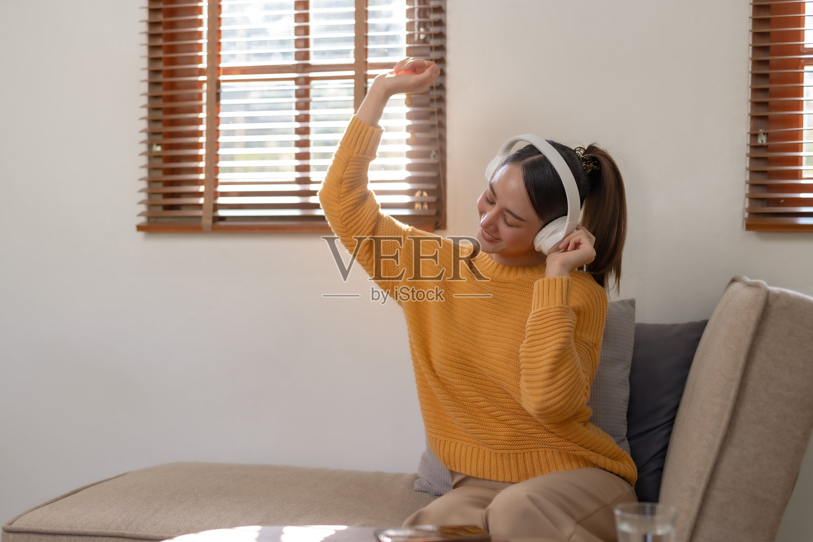 可爱的亚洲年轻女子戴着耳机坐在沙发上听音乐快乐和放松在家听音乐。照片摄影图片