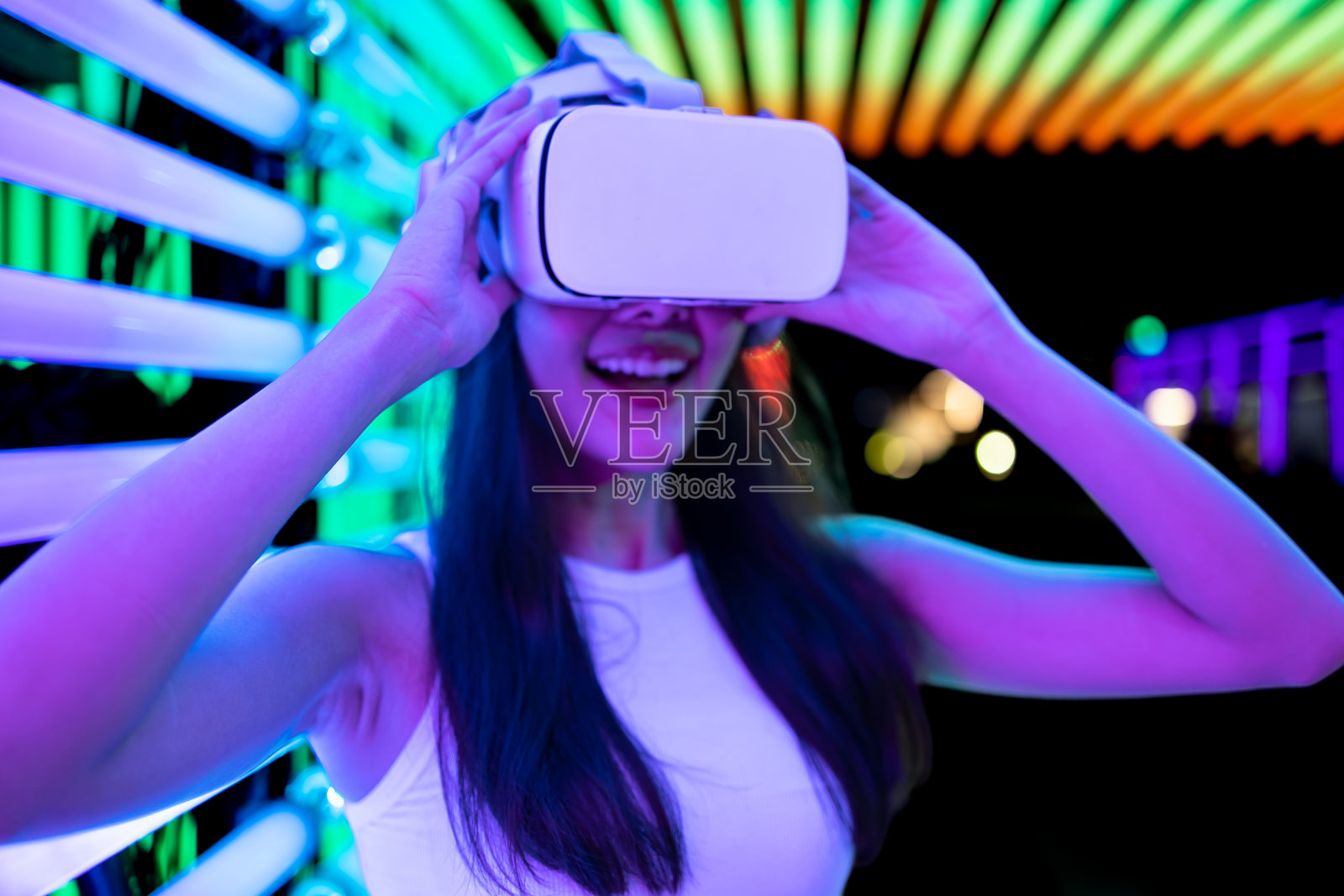 亚洲女人玩游戏与霓虹灯墙的背景。虚拟现实的概念，模拟，游戏和未来技术。照片摄影图片