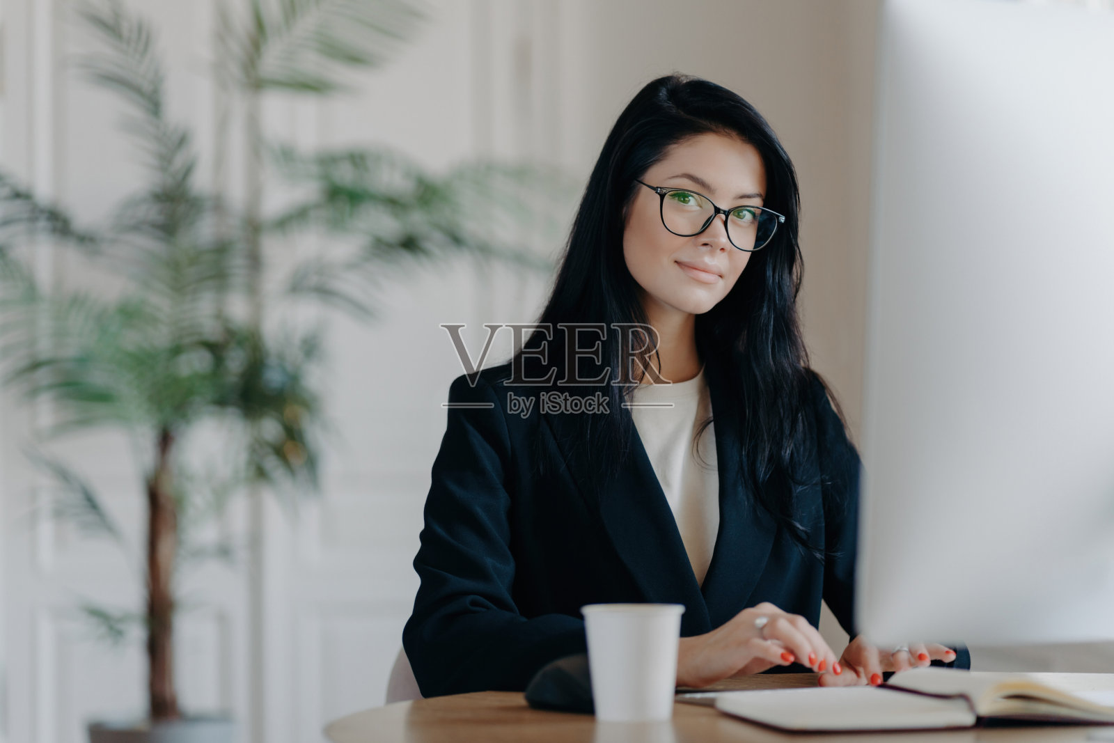 严肃成功的女性上班族，穿着正装，戴着眼镜，忙于网上工作，在桌面摆姿势，在电脑上工作，阅读业务新产品或观看教程，享受工作过程。照片摄影图片