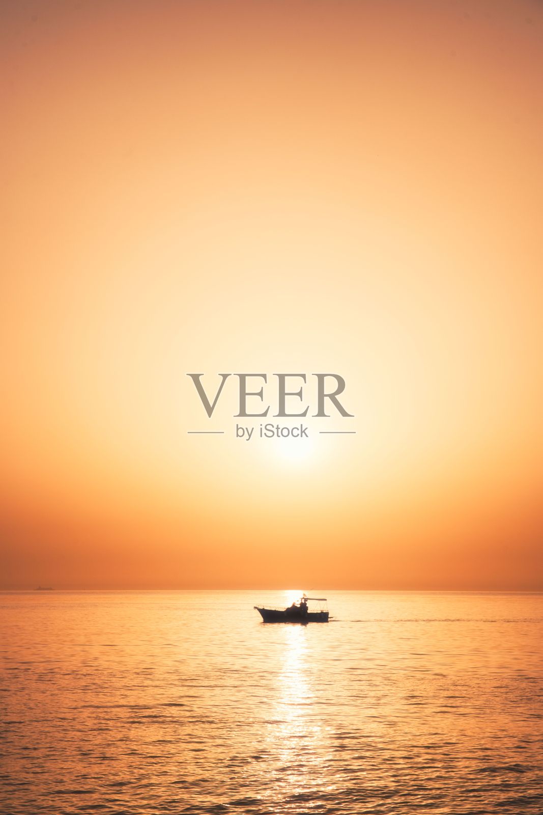 太阳落在平静的海面上，一只小船驶过海面照片摄影图片