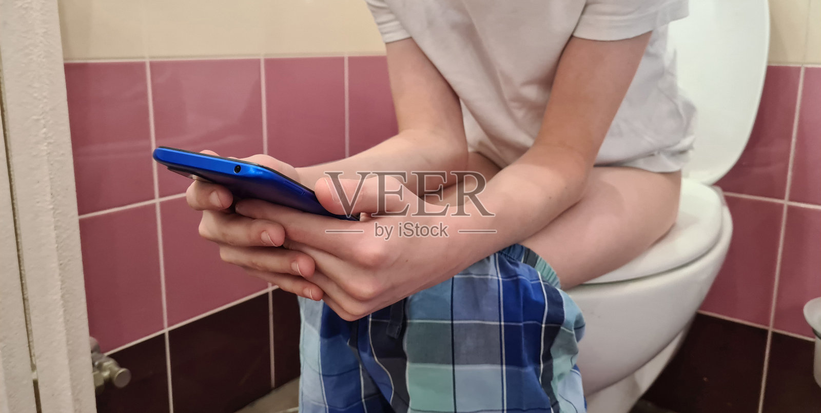 少年男孩坐在马桶座圈上玩手机照片摄影图片