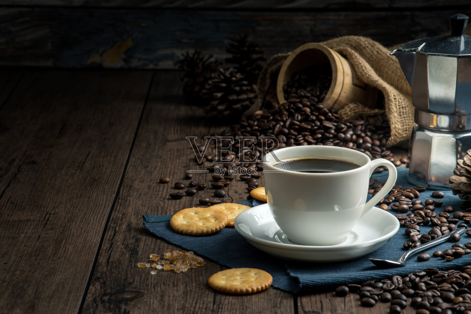 白色的咖啡杯里装着热咖啡，周围放着许多咖啡豆，木桌上放着饼干照片摄影图片