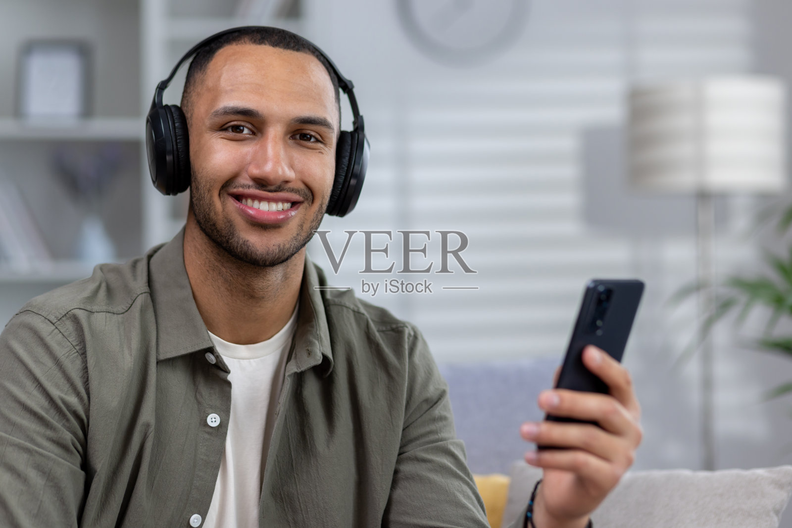 戴着耳机，用手机App听音乐或播客的非裔美国年轻男子肖像。正在进行视频通话，面带微笑看向镜头照片摄影图片