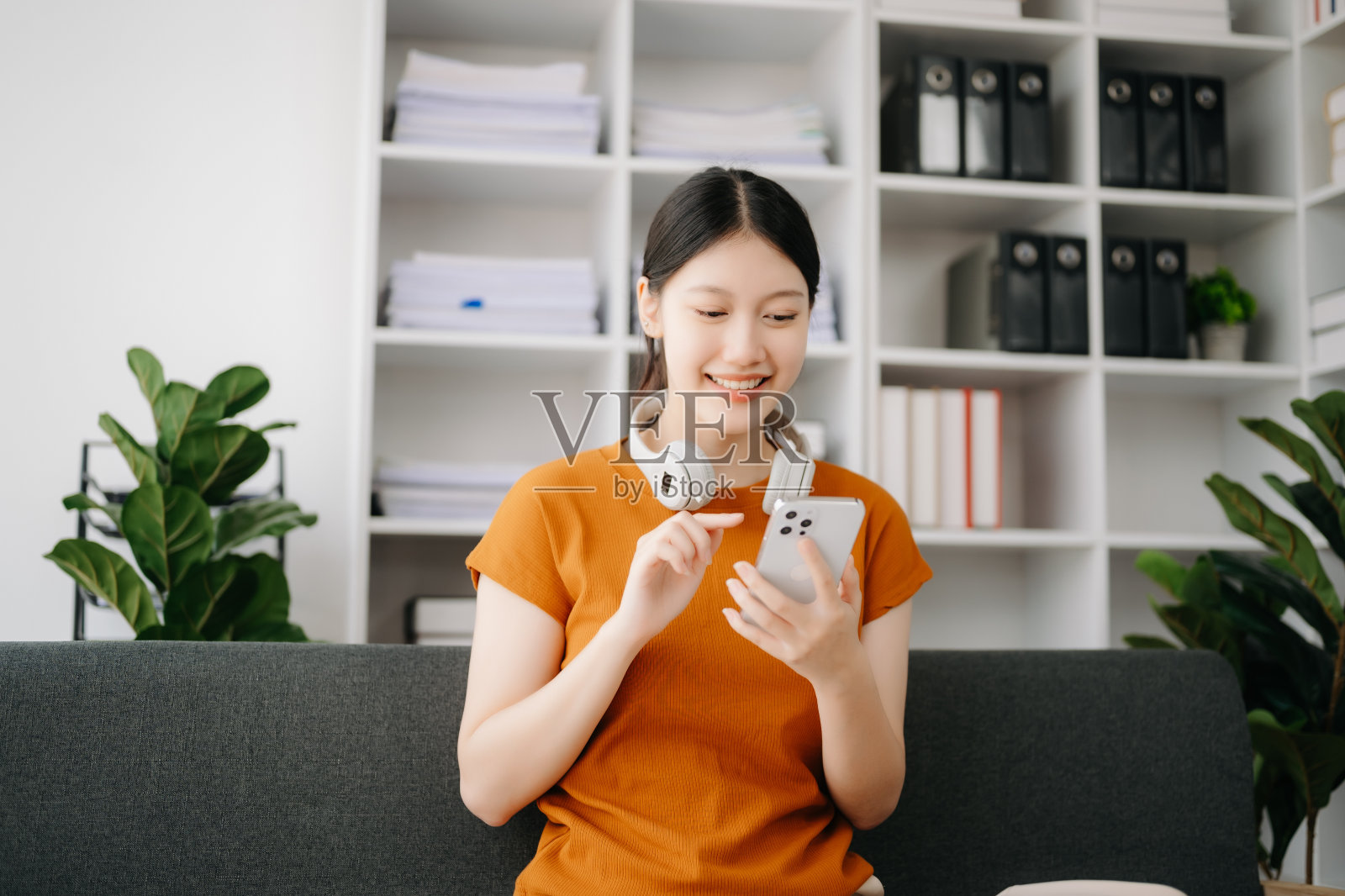 亚洲年轻女性坐在家里的沙发上使用智能手机和平板电脑照片摄影图片