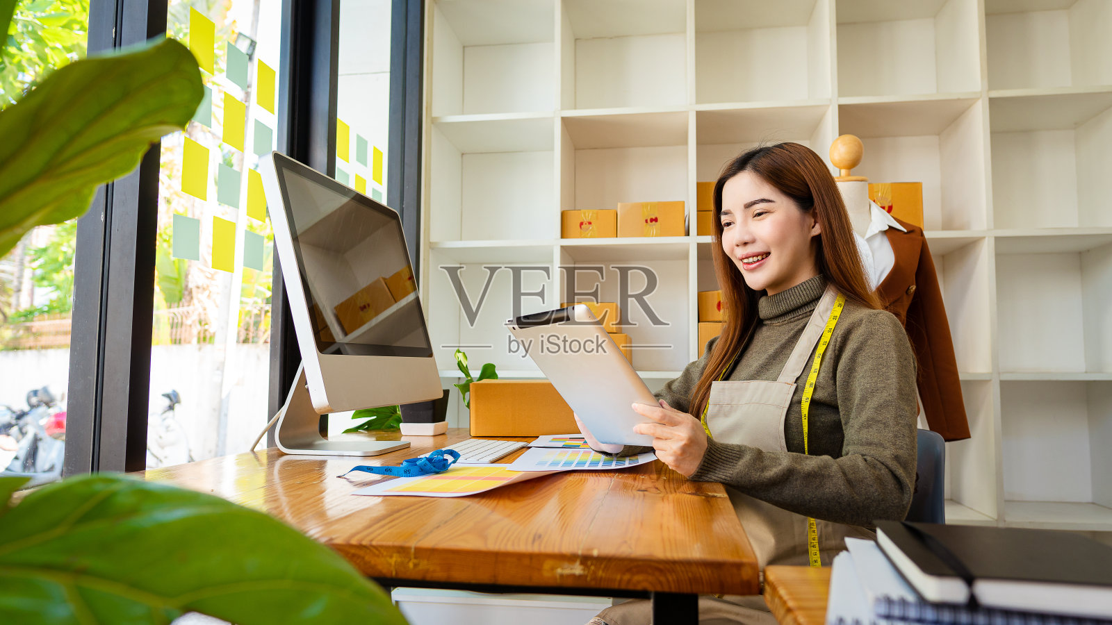 成功的时装设计师迷人的亚洲女性工作设计服装与数字和彩色纸与笔记本电脑在桌子上和后面的盒子。中小企业老板美丽的女人在工作室工作照片摄影图片