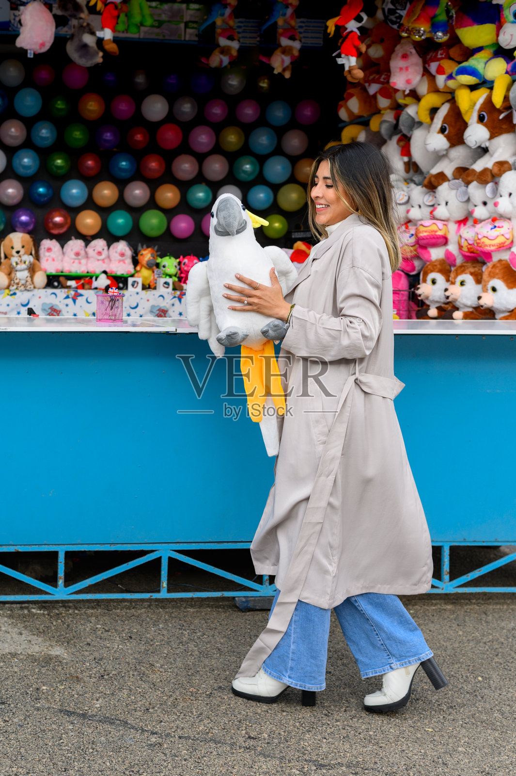 快乐的女人和毛绒玩具鹦鹉附近气球飞镖。照片摄影图片