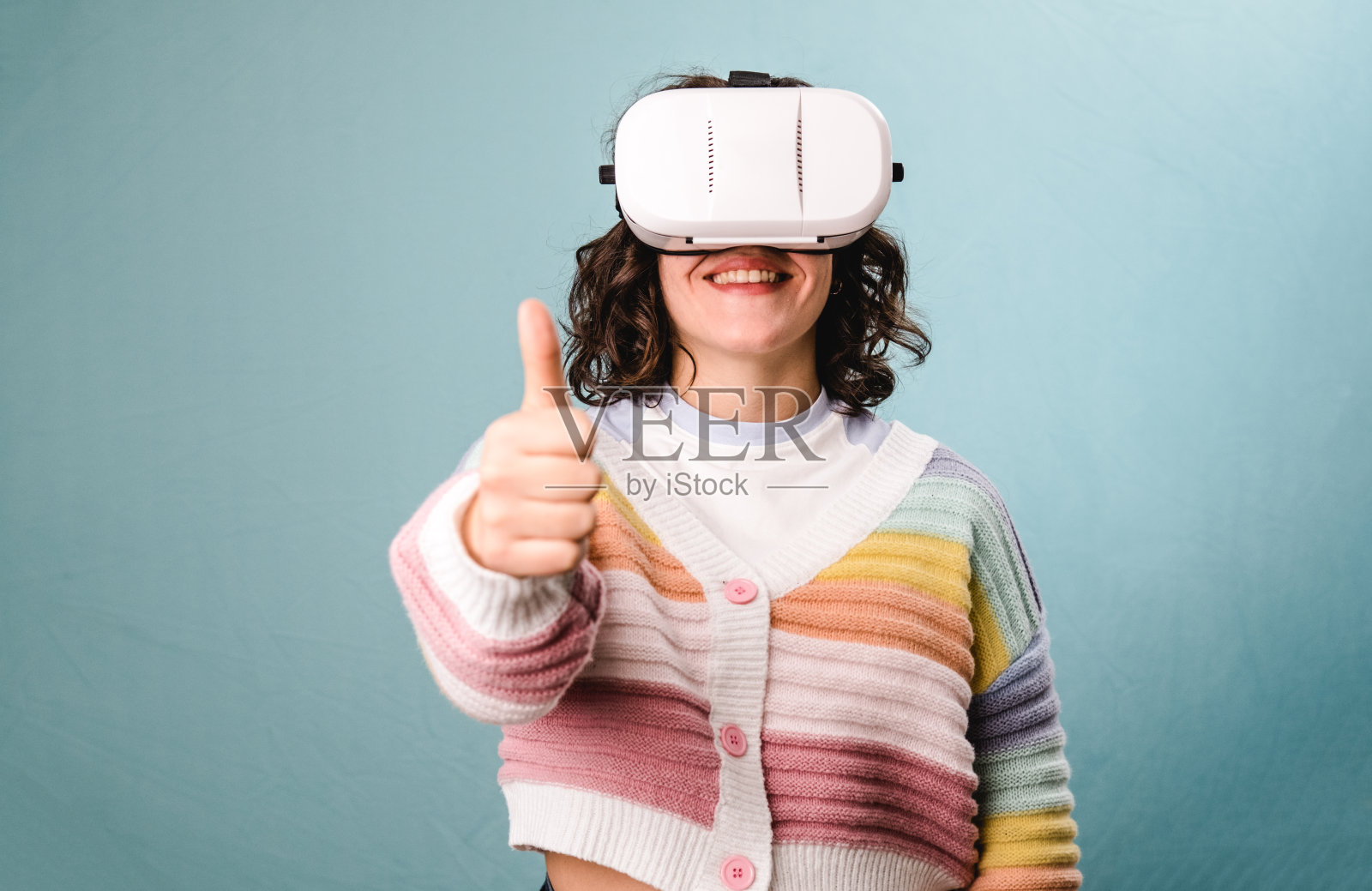 女性在蓝色背景下使用VR虚拟现实头盔时竖起大拇指。照片摄影图片