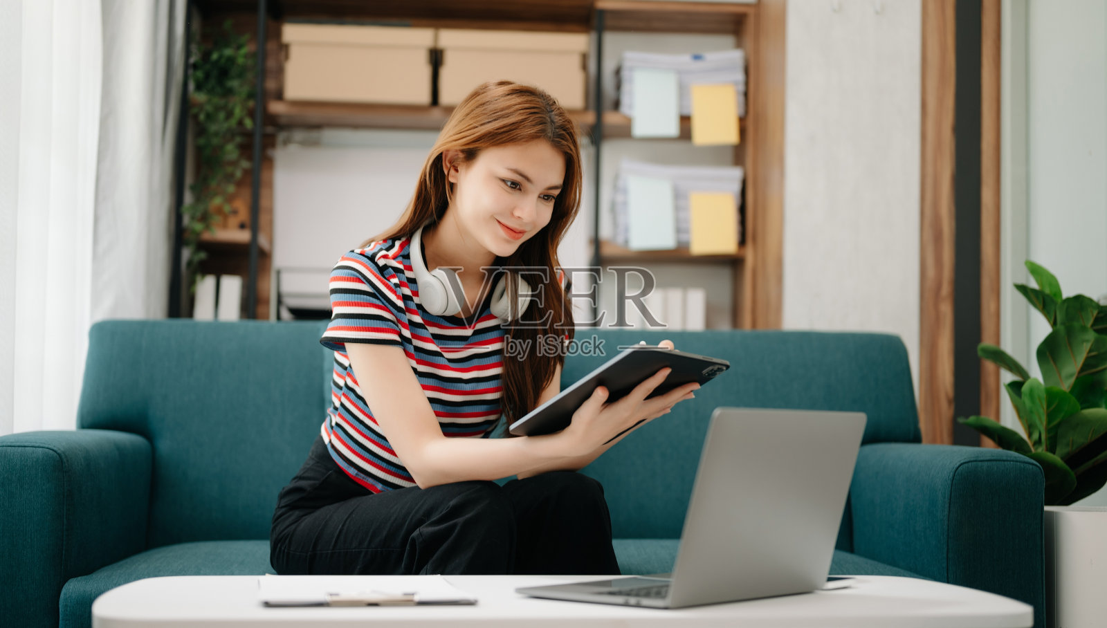 在亚洲女孩图书馆，女学生坐在沙发上用笔记本电脑和平板电脑上网搜索信息。照片摄影图片