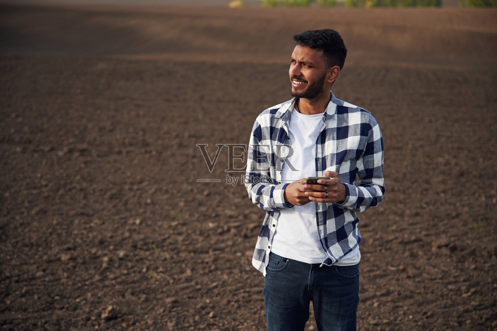 站着拿着智能手机。种植场。英俊的印度男人照片摄影图片