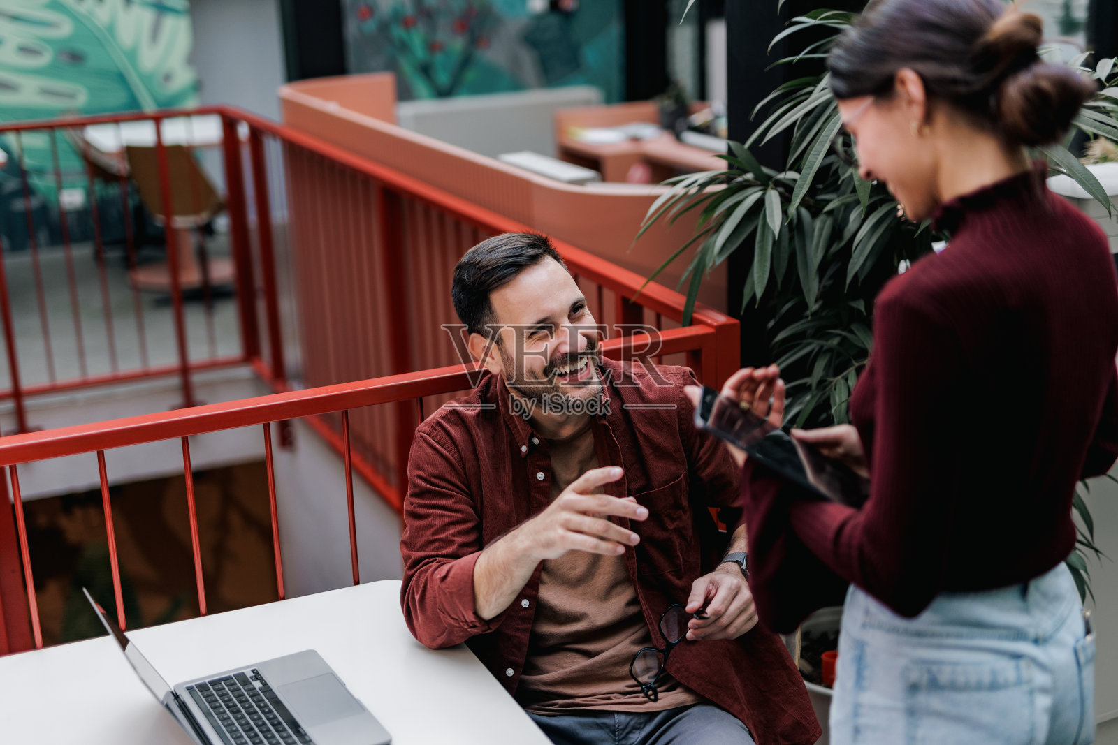微笑的商人坐着和站在他旁边的女客户交谈。照片摄影图片