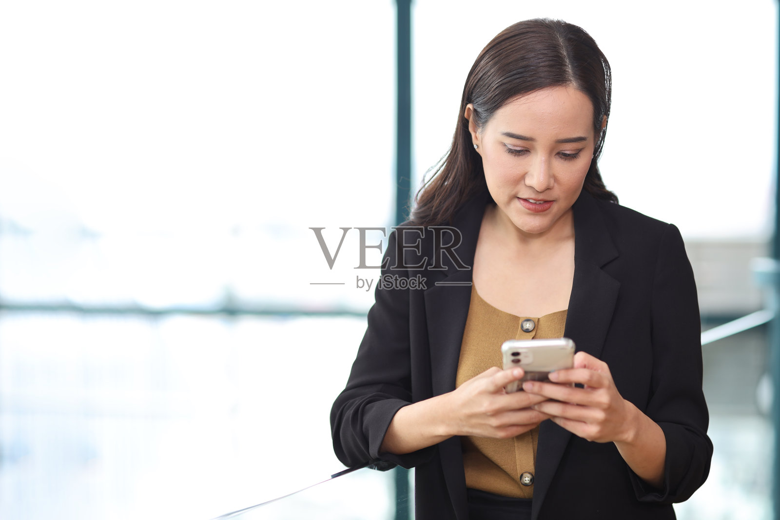 自信的年轻亚洲女商人在现代办公大楼和城市背景下使用智能手机进行商务会议，脸上带着快乐的微笑，研究和规划工作照片摄影图片