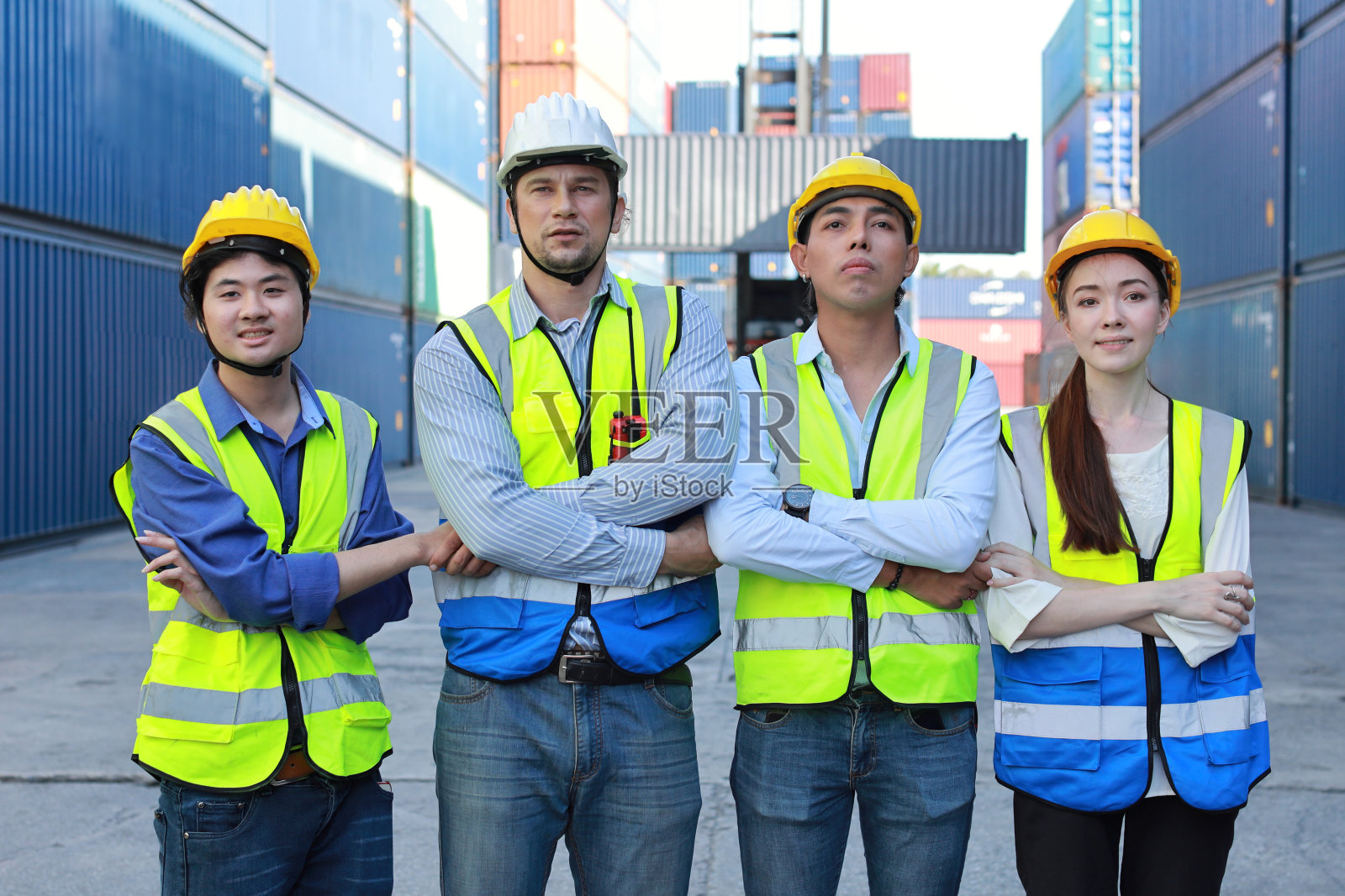 多民族技术人员、工程师和商人身穿防护服，头戴安全帽，双臂交叉，在集装箱货物现场共同庆祝成功或完成交易承诺照片摄影图片