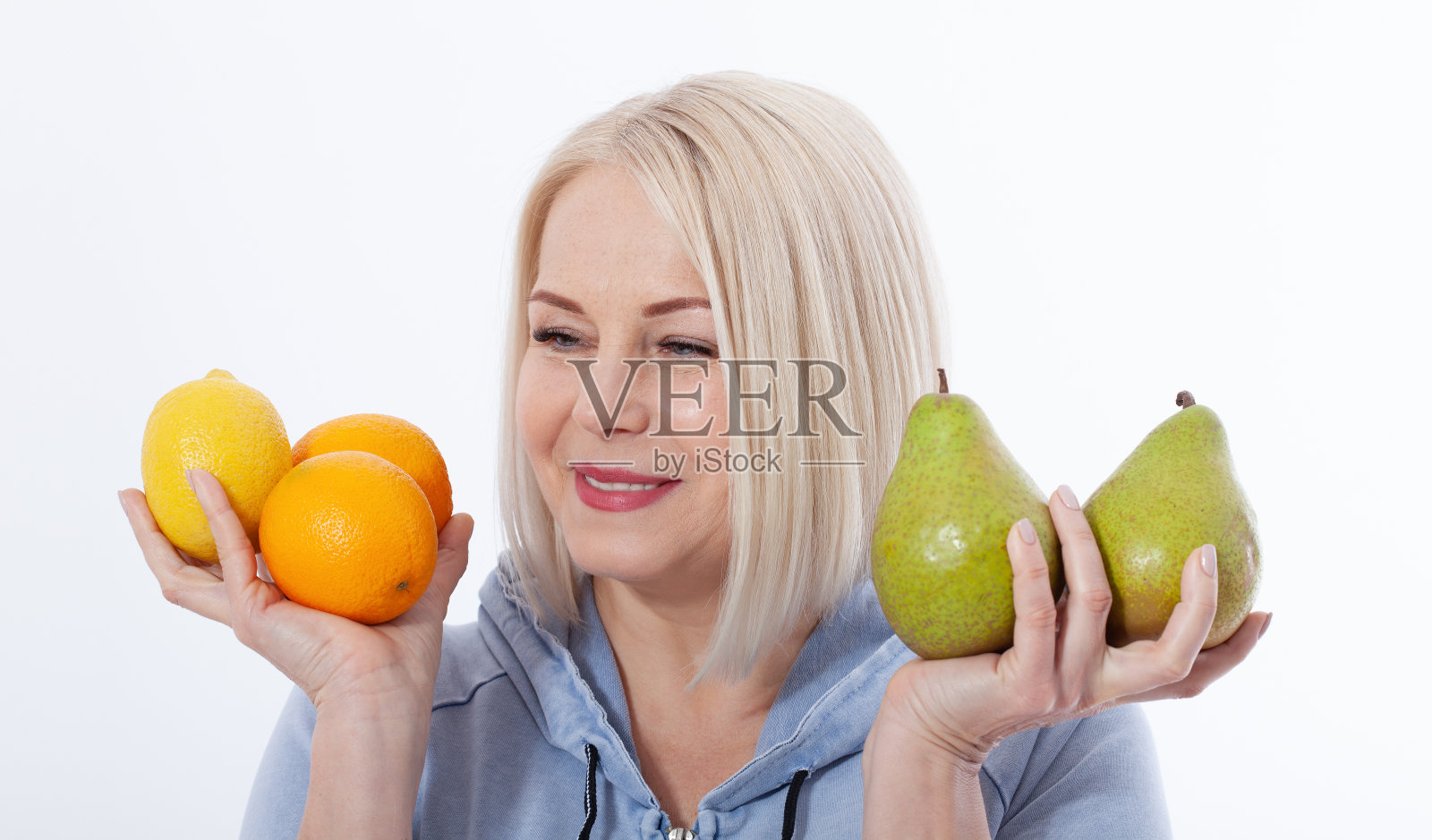 一个金发美女手里拿着两个橙子、柠檬和一个梨，这是一种富含维生素的健康饮食。概念健康食品水果照片摄影图片