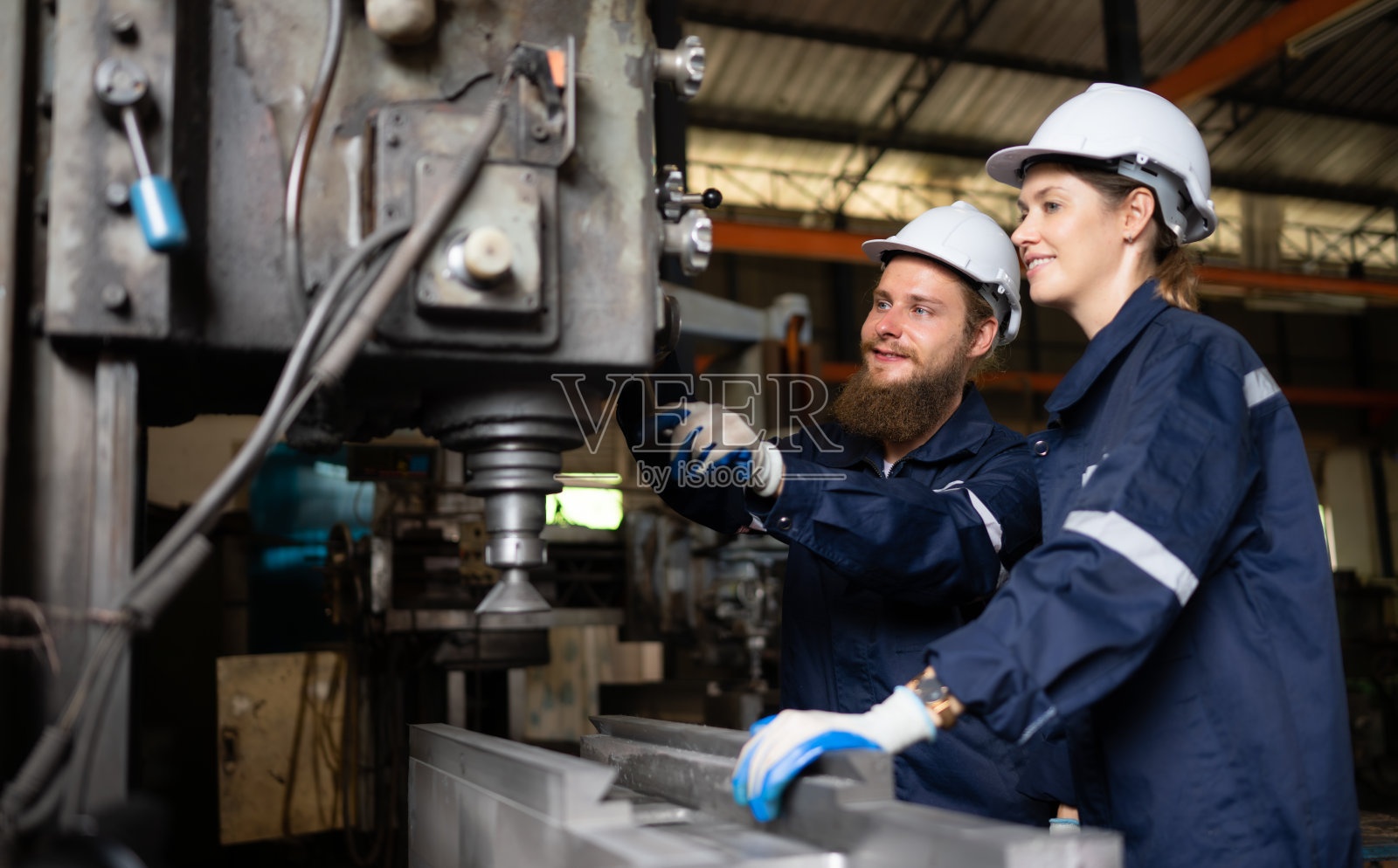 两位机械工程师正在检查一台已经使用了一段时间的旧机器的工作状况。在一个自然光照射到工作场所的工厂里照片摄影图片