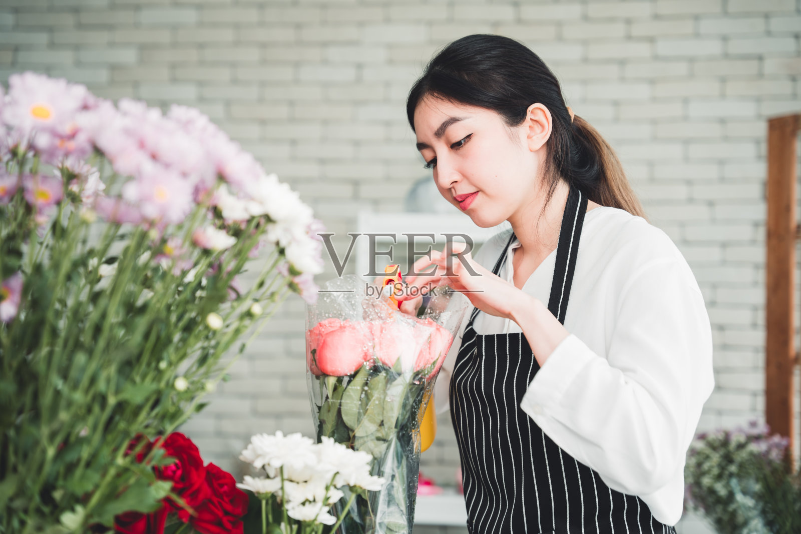 在花店里，一个年轻的女人正在照顾鲜花，轻轻地给花浇水，以增加水分，防止花朵枯萎。照片摄影图片
