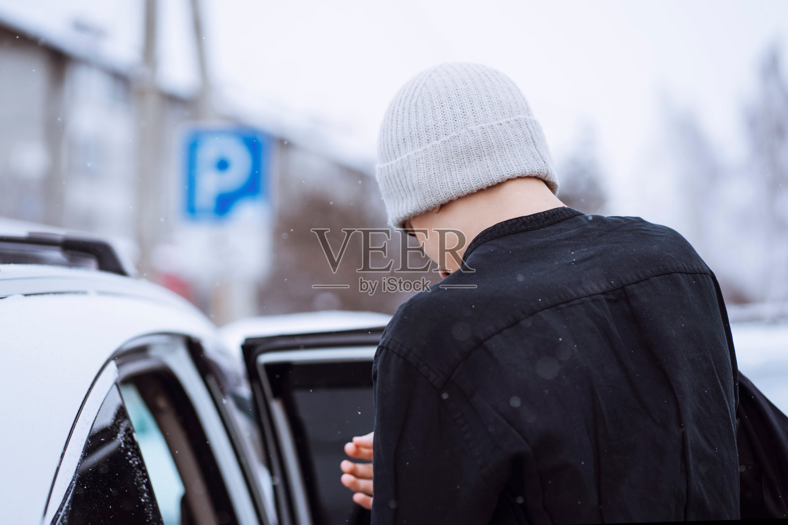 一个人在冬天的停车场，车旁边。照片摄影图片
