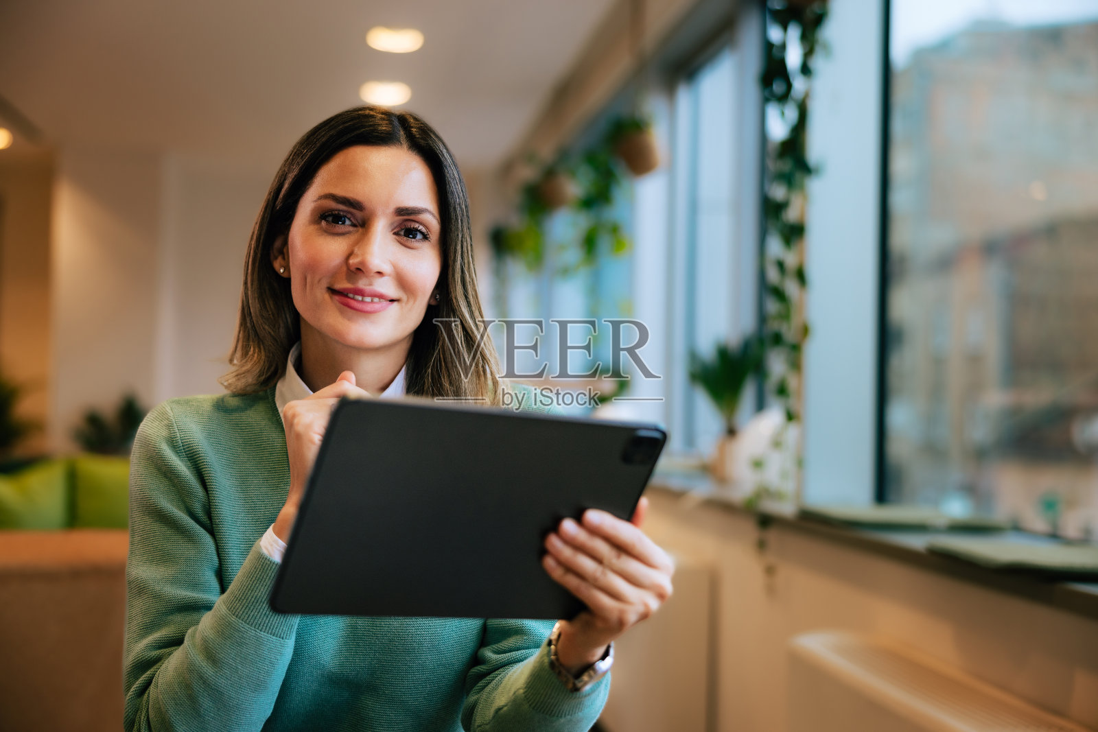 一个女商人坐在办公室里，手里拿着数码平板电脑。照片摄影图片