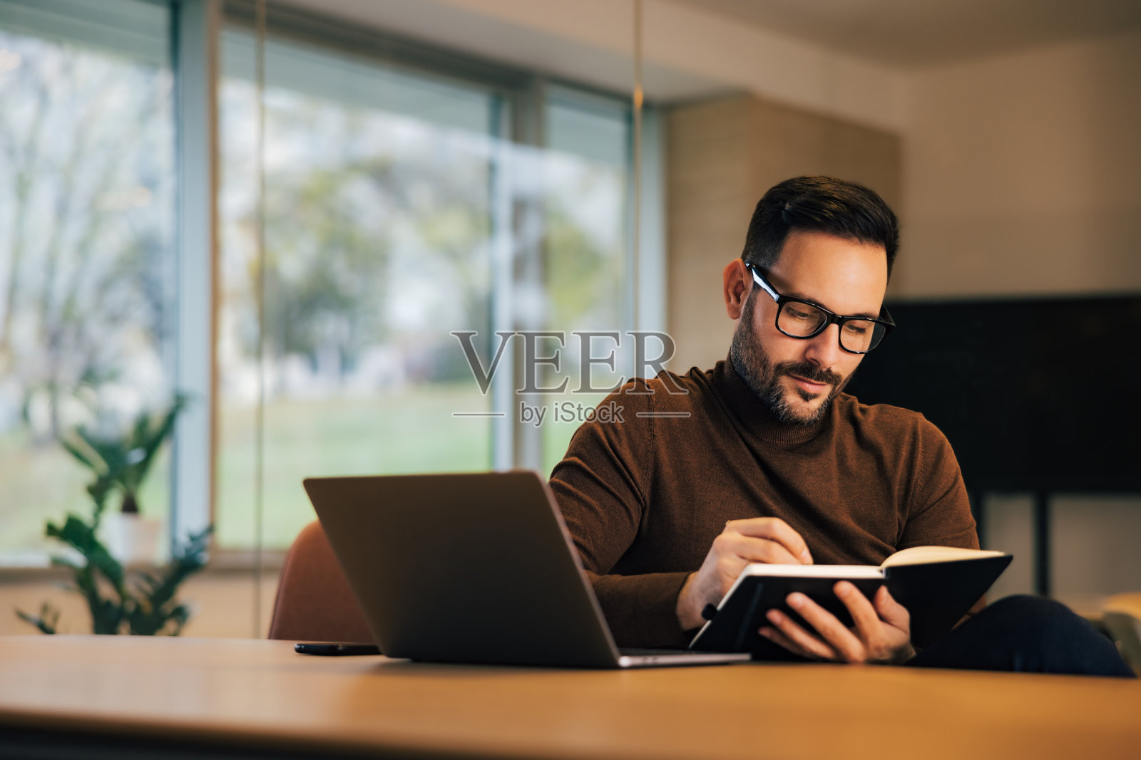 专注的男性雇主在办公室里对着笔记本电脑做笔记。照片摄影图片
