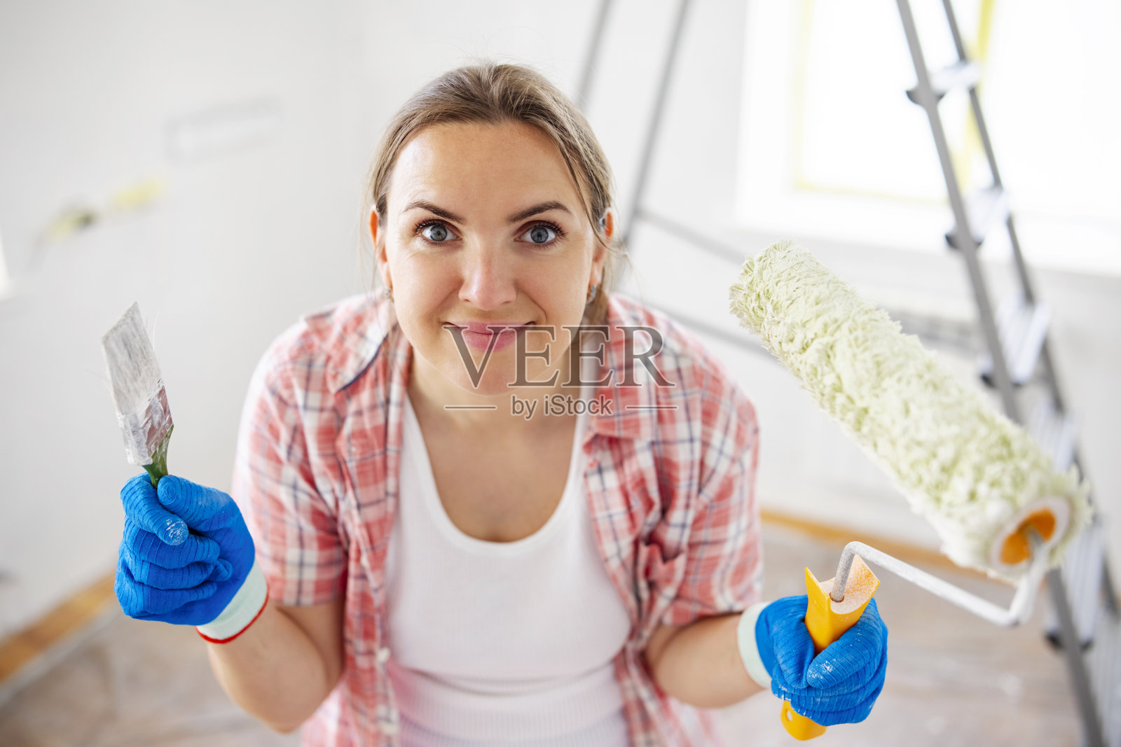 在粉刷完房间的墙壁后，正拿着脏滚筒和刷子的女人照片摄影图片