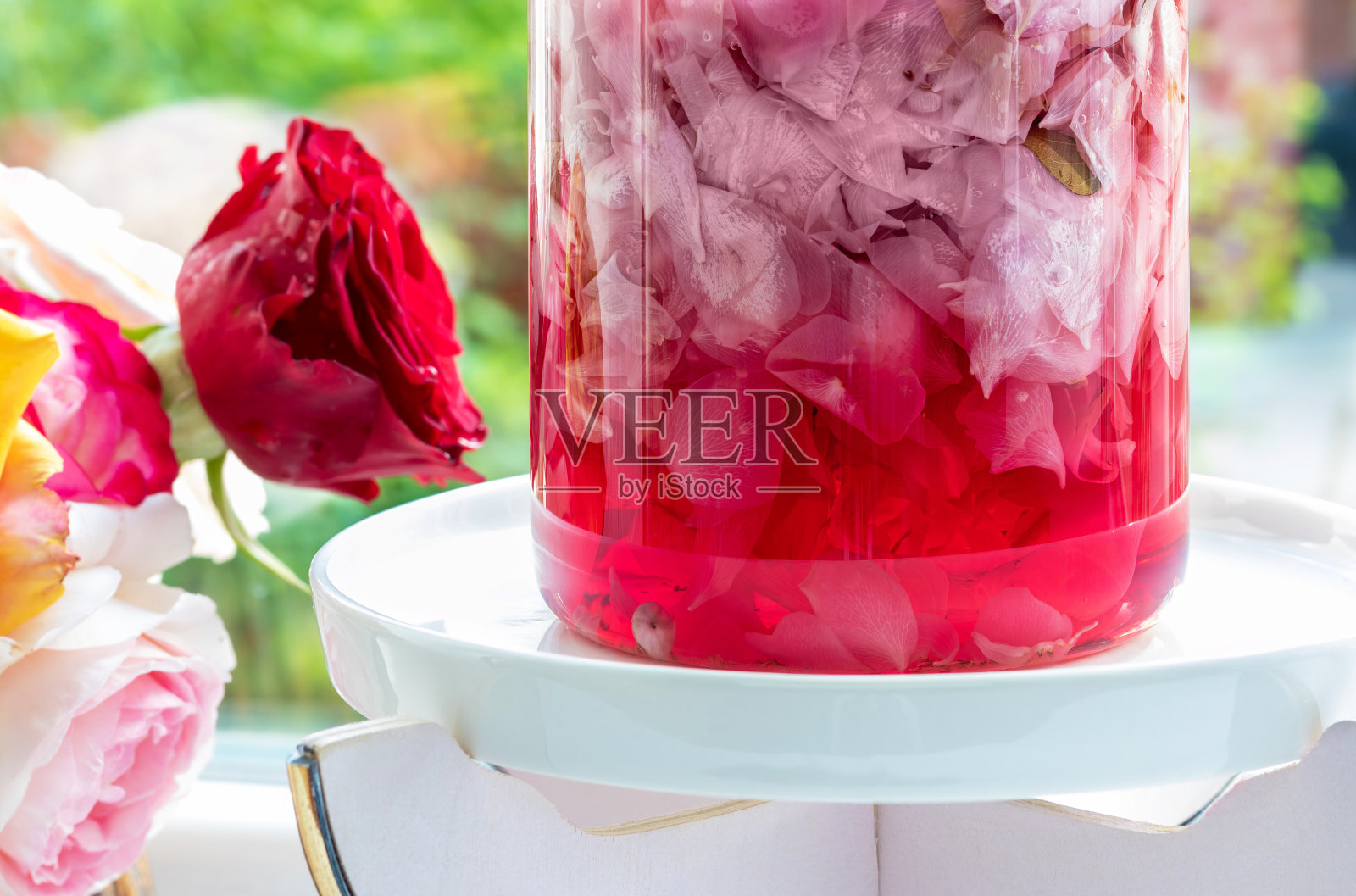 玫瑰水。特写镜头。配制玫瑰水时，将玫瑰花瓣浸入玻璃烧瓶中。照片摄影图片