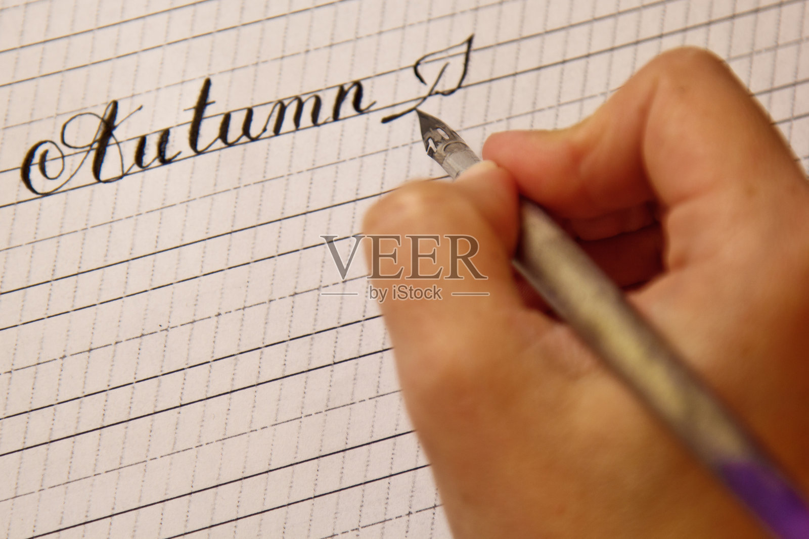 女人的手用墨笔在有条纹的白纸上写着秋天这个词。办公桌上的文具近距离俯视图。拼写课和书法练习。模板，布局，背景照片摄影图片