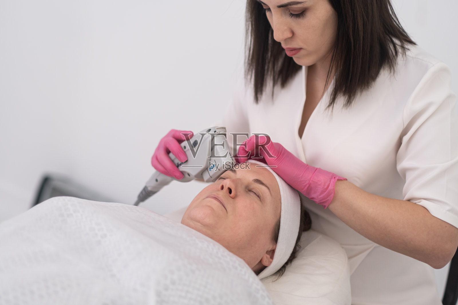 女美容师正在进行超声面部拉皮美容，病人舒适地躺着照片摄影图片