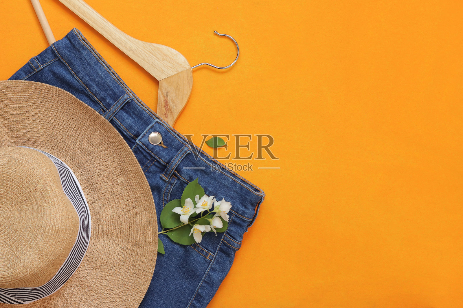 夏天的照片，衣服在明亮的橙色背景。夏帽，牛仔短裤和衣架。副本的空间。俯视图，平铺。时尚与风格照片摄影图片