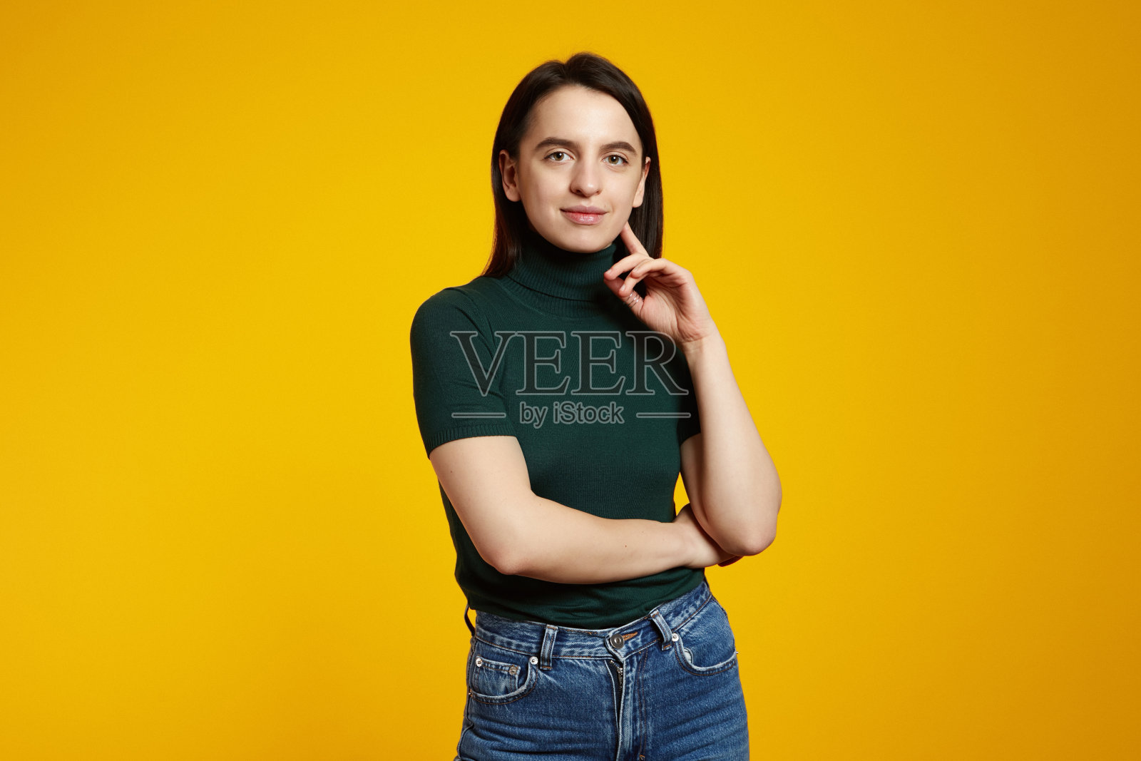 年轻的女孩穿着绿色的t恤，手指放在脸颊上，孤立的黄色背景照片摄影图片