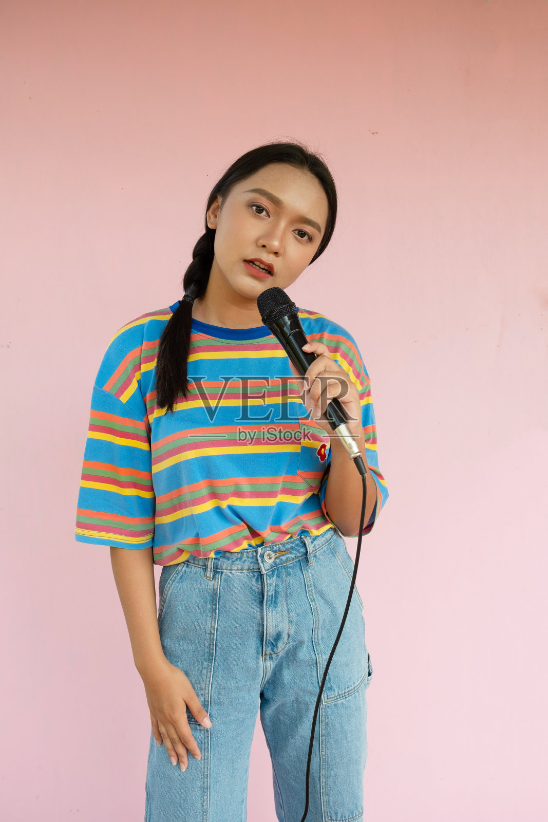 这个女孩站在粉红色的背景上唱歌。照片摄影图片