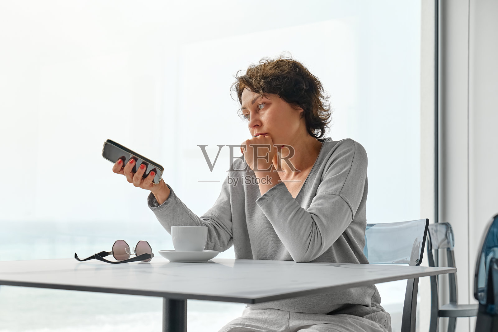 早晨，一位忧心忡忡的女子在咖啡馆里一边喝咖啡，一边查看手机社交网络。照片摄影图片