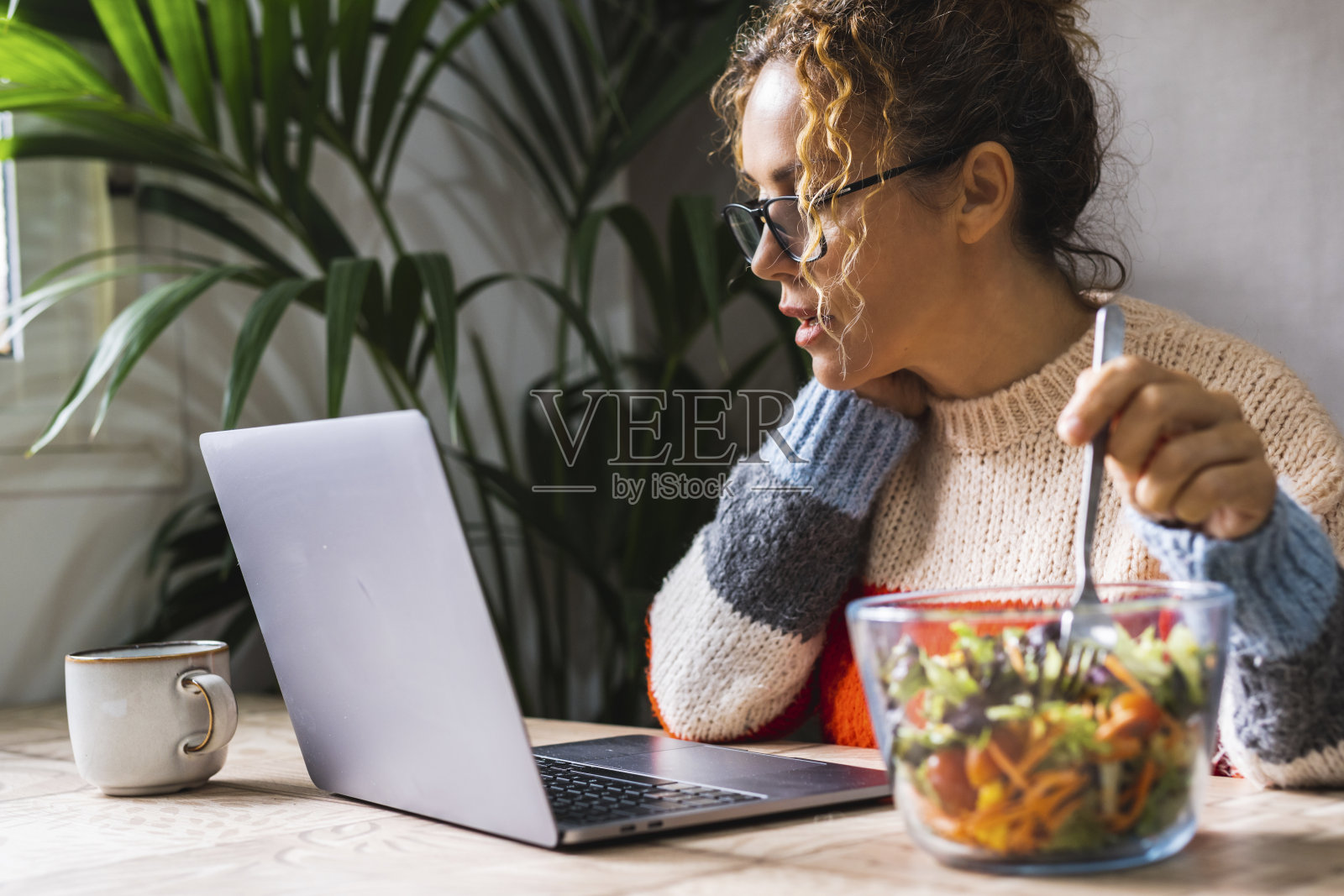 一个忙于工作的女人一边在电脑前工作，一边吃着健康的沙拉。工作时间的午休时间。健康的女性生活方式。办公室、家庭、工作场所照片摄影图片