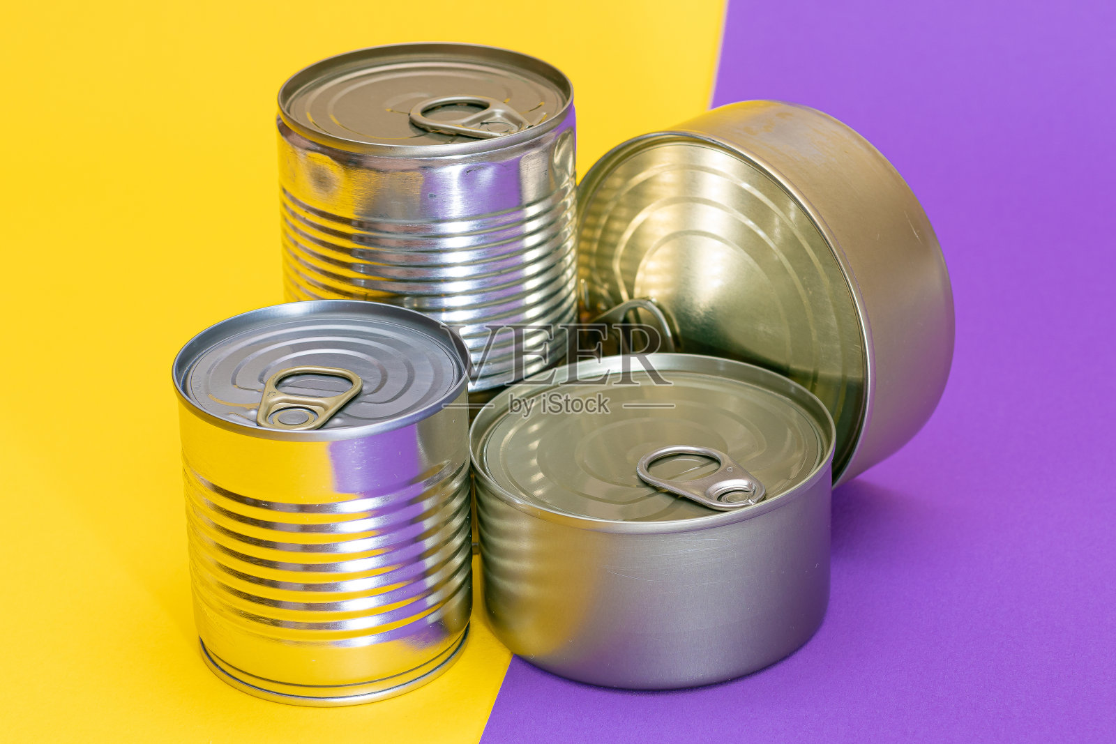 一组堆叠的锡罐与空白边缘在分裂的黄色和紫色背景照片摄影图片
