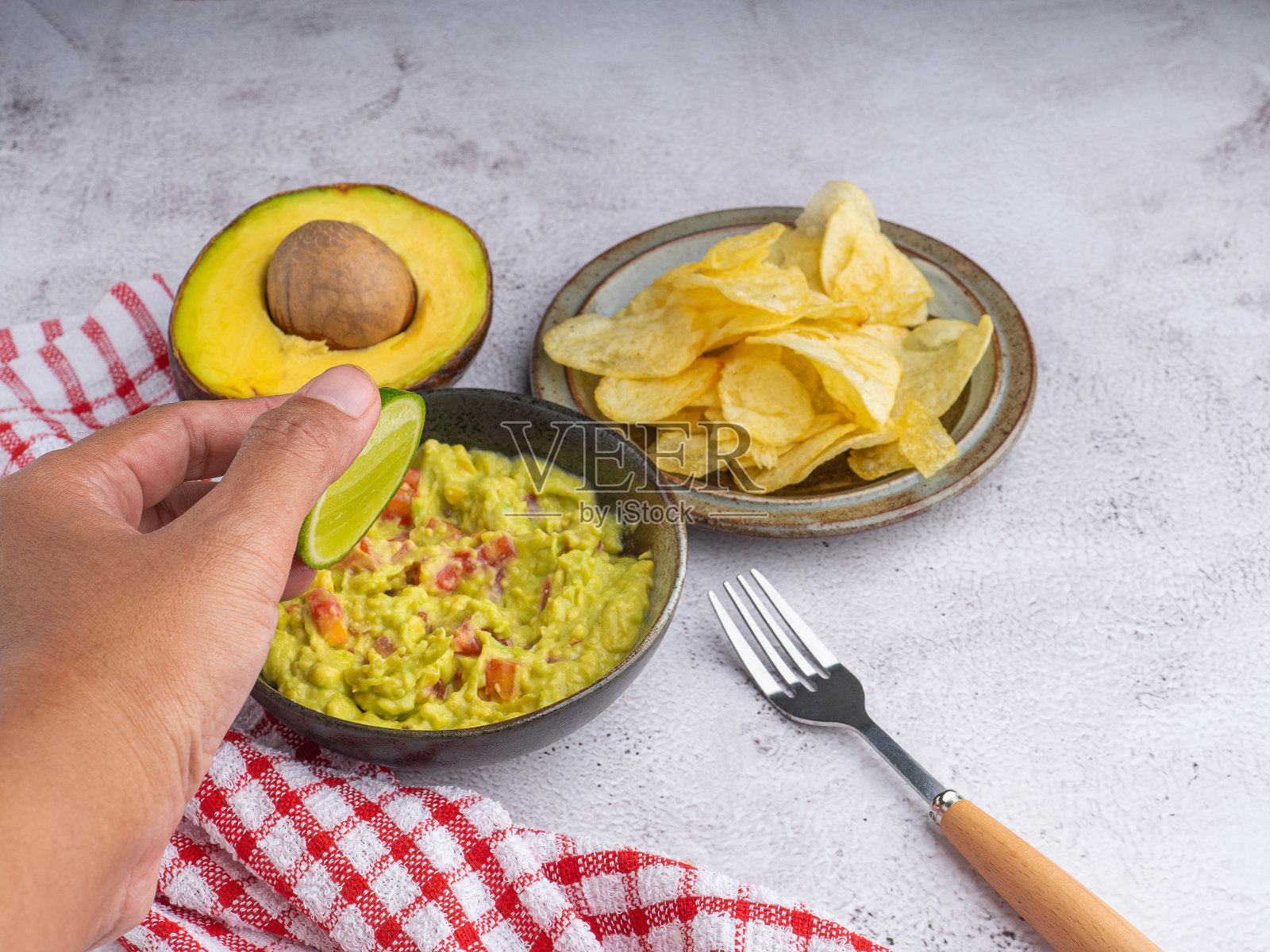 新鲜的鳄梨酱碗和薯片放在灰色石头背景上的盘子里。照片摄影图片