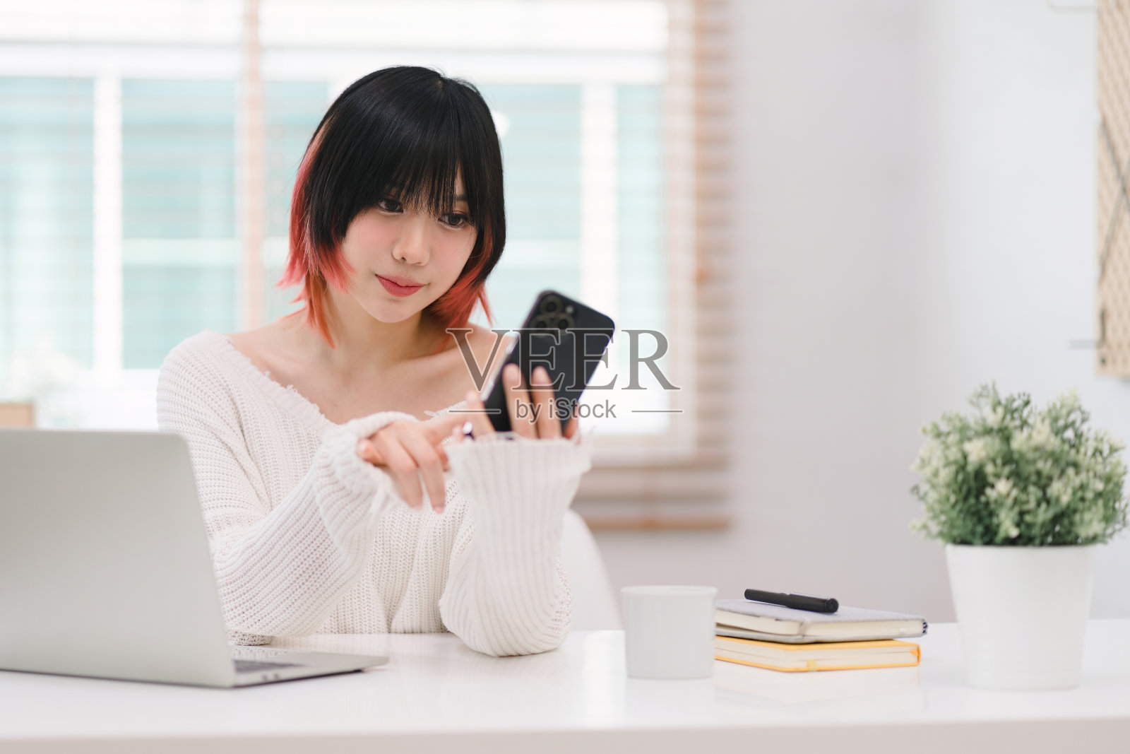 在家里舒适的客厅里，一位漂亮的年轻女子用灵巧的手指全神贯注地在智能手机上发信息。照片摄影图片