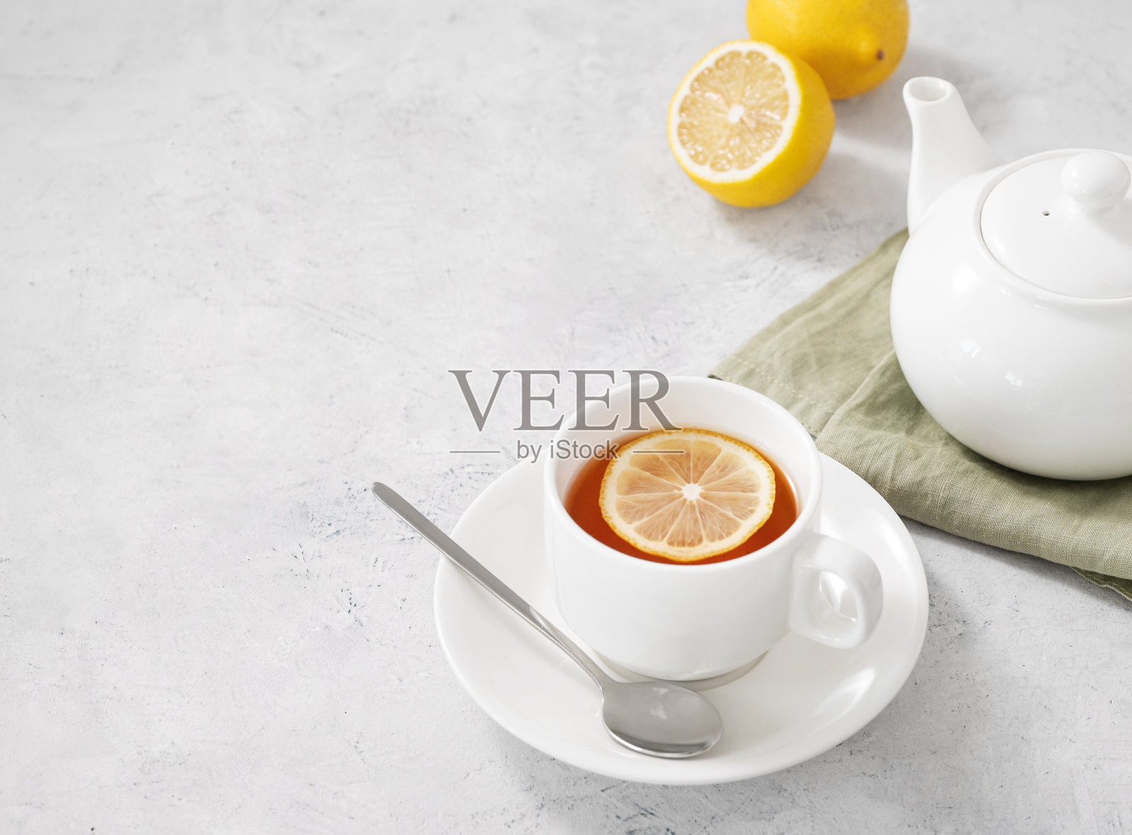 一杯带有柠檬和茶壶的草药茶，背景较浅。健康排毒饮品理念。照片摄影图片