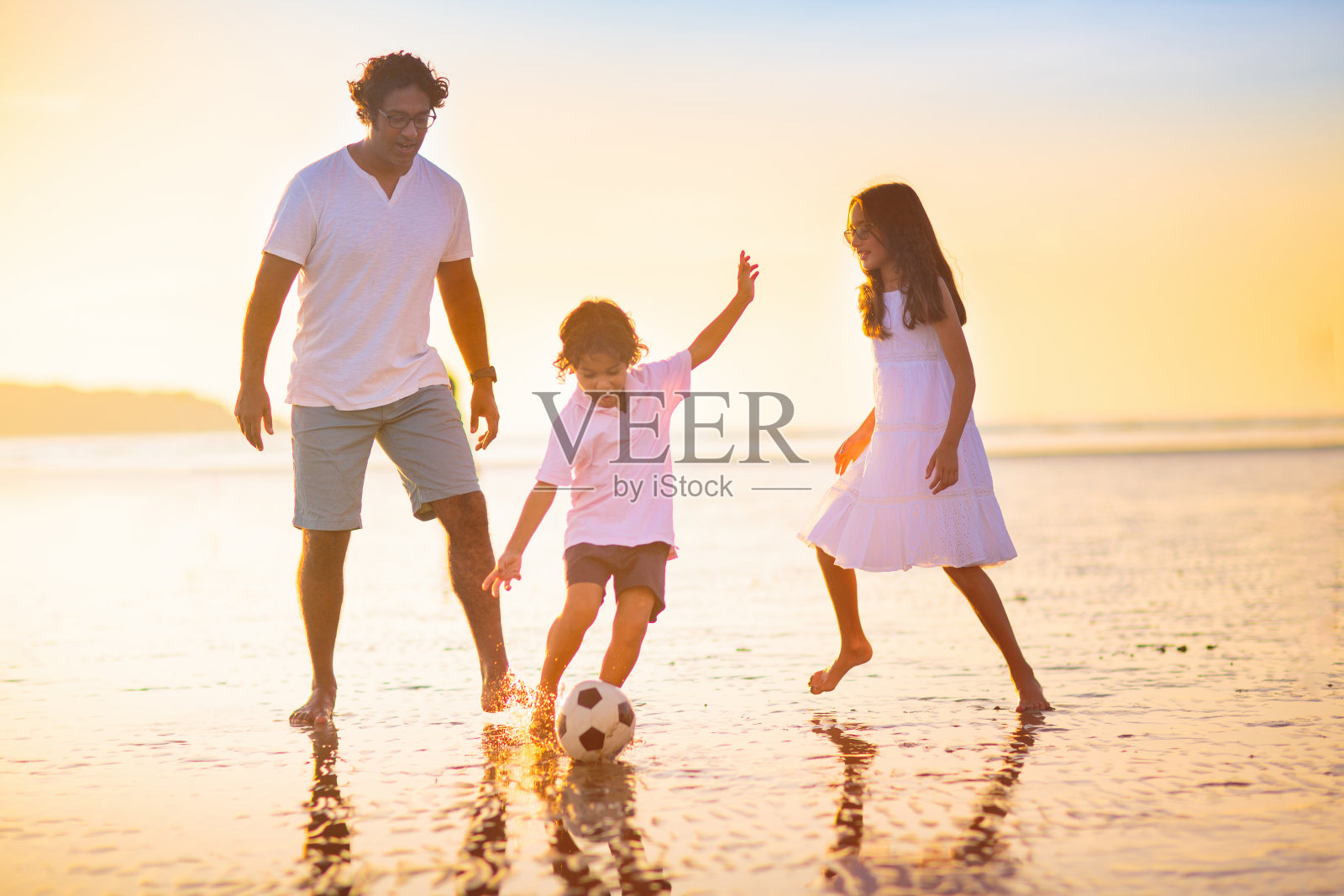 日落时分，孩子们在热带海滩上踢足球照片摄影图片