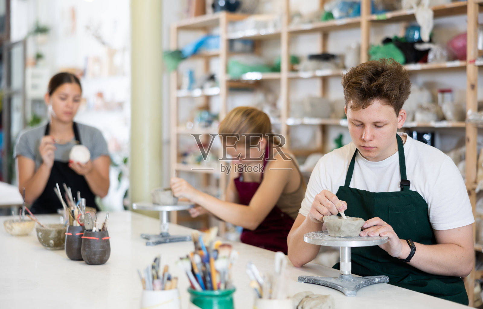 十几岁的男孩系着围裙在车间里制作粘土陶器照片摄影图片