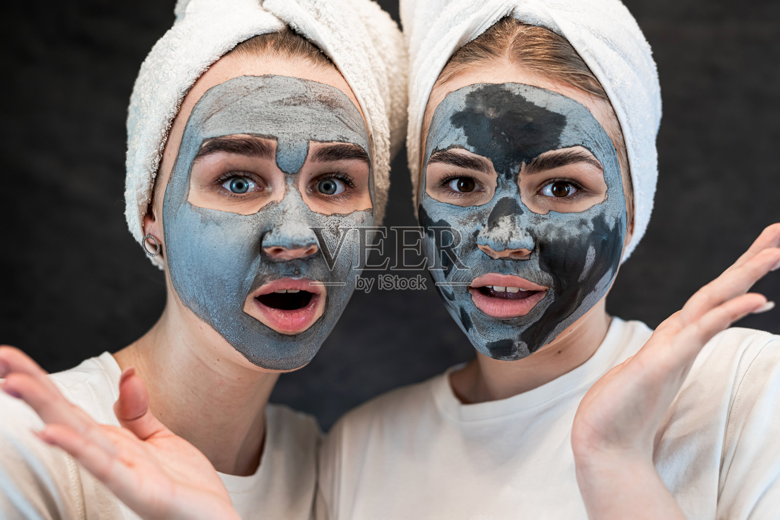 快乐的年轻白人妹妹，穿着白色的t恤，毛巾，脸上戴着木炭面具，孤立在黑色上照片摄影图片