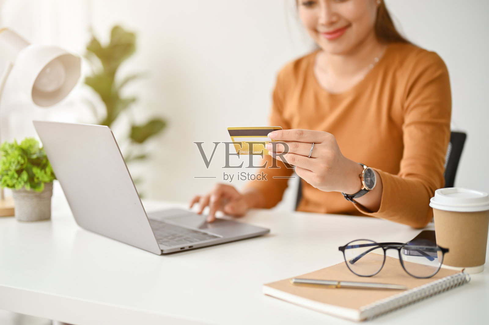 一个女人坐在桌子旁，手里拿着一张信用卡，正在用她的笔记本电脑照片摄影图片