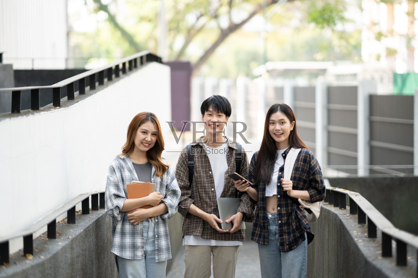 一群兴高采烈的学生带着笔记本和手提电脑，走进教室。照片摄影图片