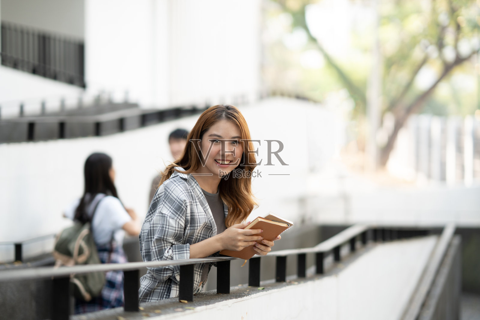 可爱的年轻学生拿着书站在楼前。照片摄影图片