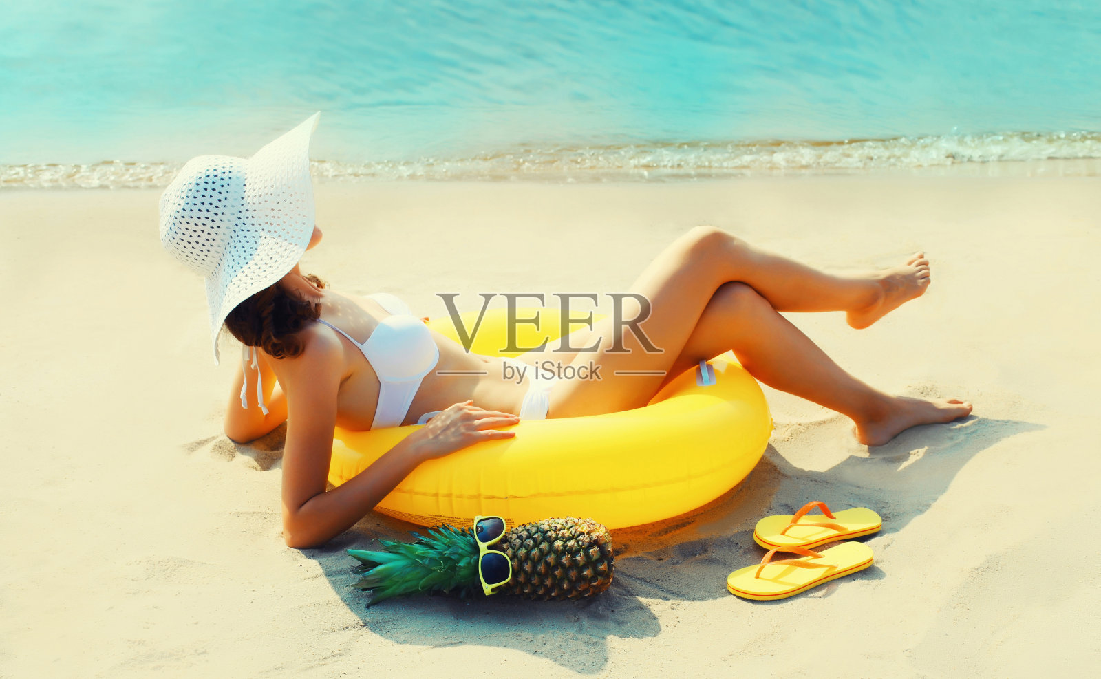 暑假，快乐放松的年轻女子躺在沙滩上，在沙滩上游泳充气环在大海的背景照片摄影图片