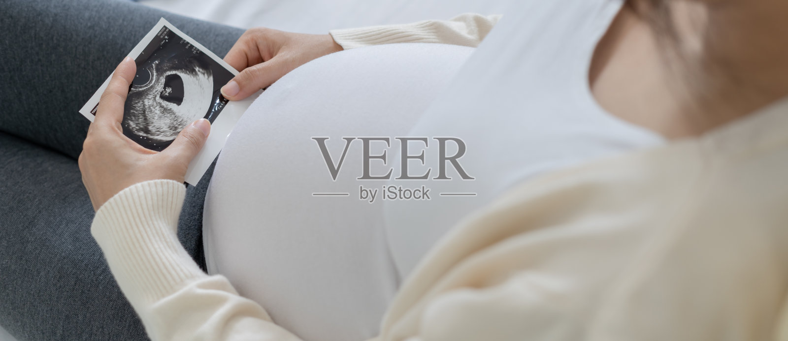 一位孕妇正在看胎儿的超声波照片。妈妈轻轻地摸了摸婴儿的肚子。快乐，家庭，成长，怀孕，享受，准备新生儿，照顾，保健，肚子。照片摄影图片