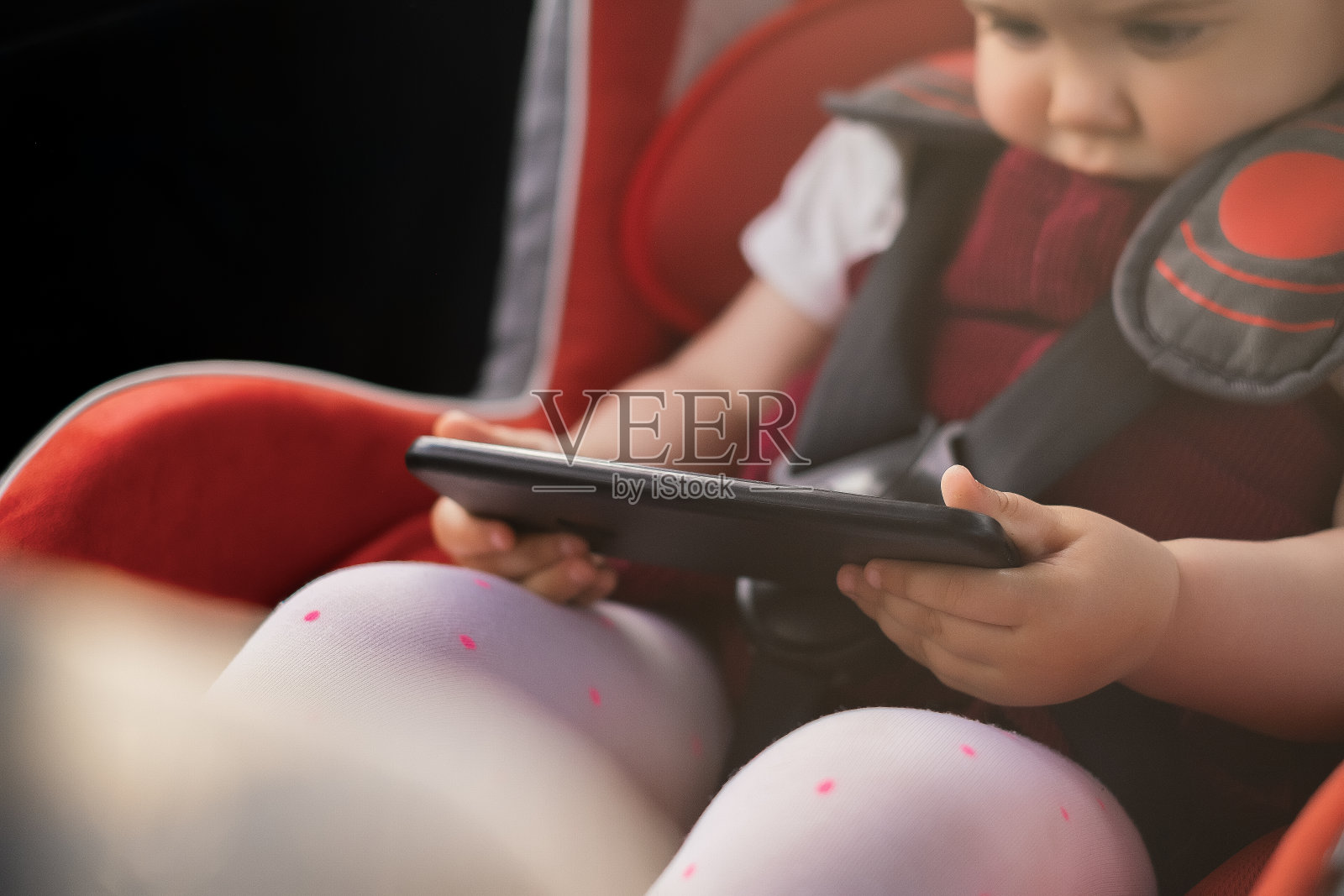 孩子坐在汽车座椅上，手里拿着手机，在手机上看动画片，孩子在玩手机，旅途上孩子的娱乐，运送孩子的安全照片摄影图片