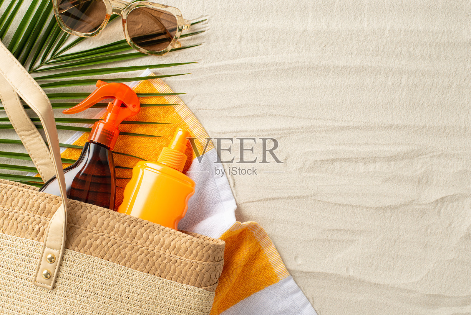 健康晒黑理念。高角度照片的柳条袋与防晒喷雾，太阳镜和棕榈叶在沙滩毛巾上孤立的沙滩背景与copyspace照片摄影图片