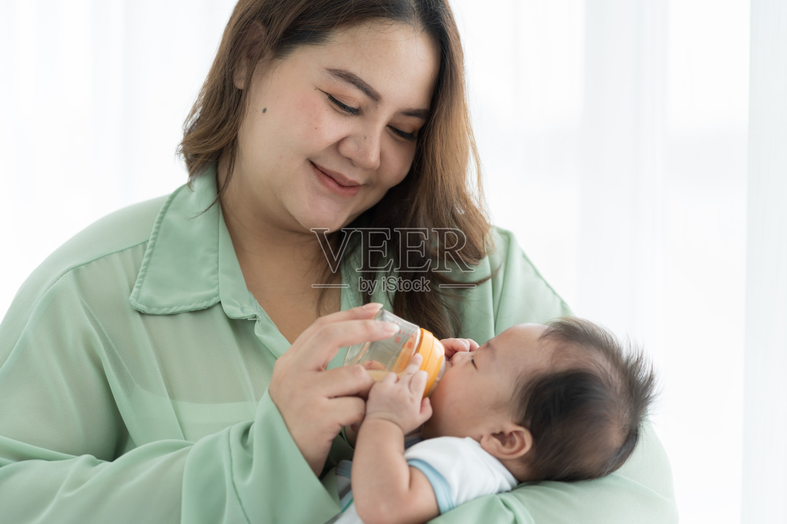 母亲抱着刚出生的婴儿用奶瓶喂奶。新生儿或婴儿在母亲拿着奶瓶时从乳头吃奶照片摄影图片