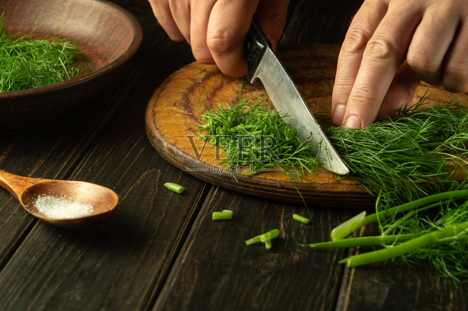 在准备国菜或素菜之前，厨师用手在厨房砧板上用刀切新鲜的茴香。农民的菜照片摄影图片