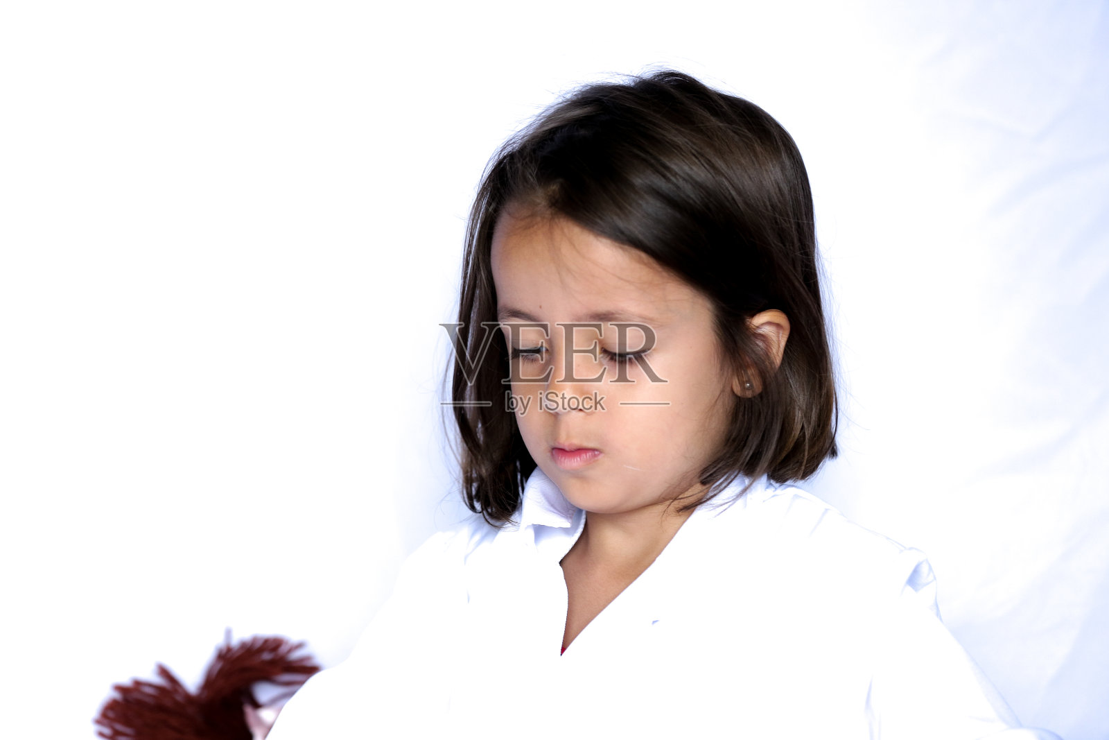 孩子戴着粉色手套，穿着医疗服，在白色背景上玩洋娃娃。照片摄影图片