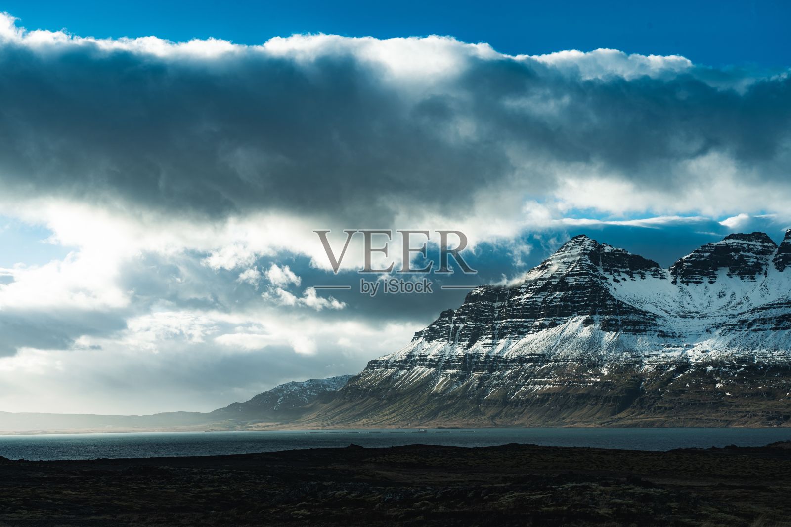 蓝色多云的天空下，冰雪覆盖着岩石悬崖的景观照片摄影图片