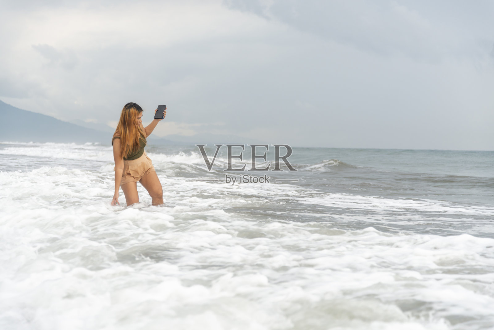 美丽的年轻菲律宾女子，在菲律宾吕宋岛赞巴莱斯的伊巴长沙滩上嬉戏地划着浅波。照片摄影图片